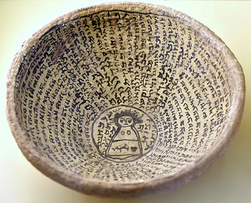 a photo of an incantation bowl from Babylon with an inscription with a human figure